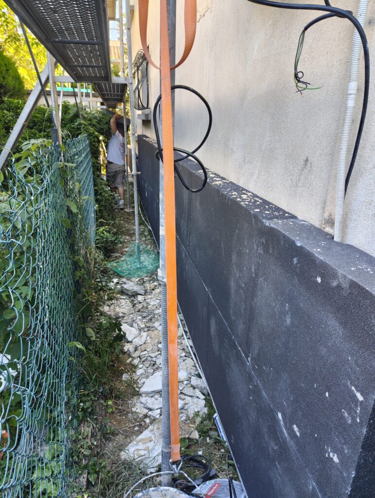 Ouvrier posant un panneau isolant noir en pied de façade dans le cadre d'un chantier d'isolation thermique par l'extérieur à Orange (Vaucluse)